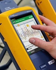 A technician’s hand pinching and zooming in on a device screen showing an OTDR trace.