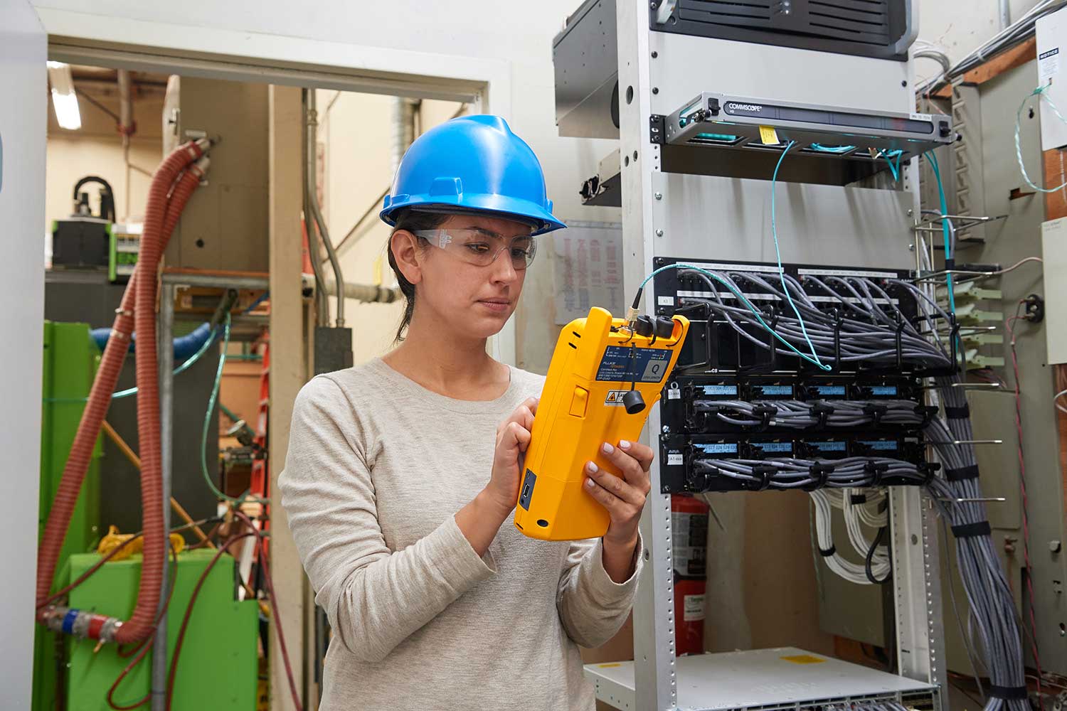 Technician in hard hat takes readings at a panel with a Fluke Networks Versiv