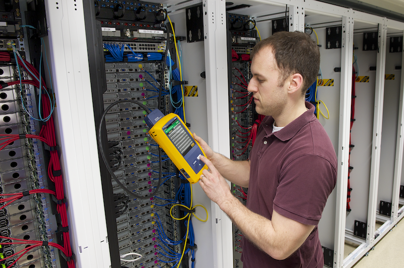 Man holding a yellow device as he tests cabling in a server rack
