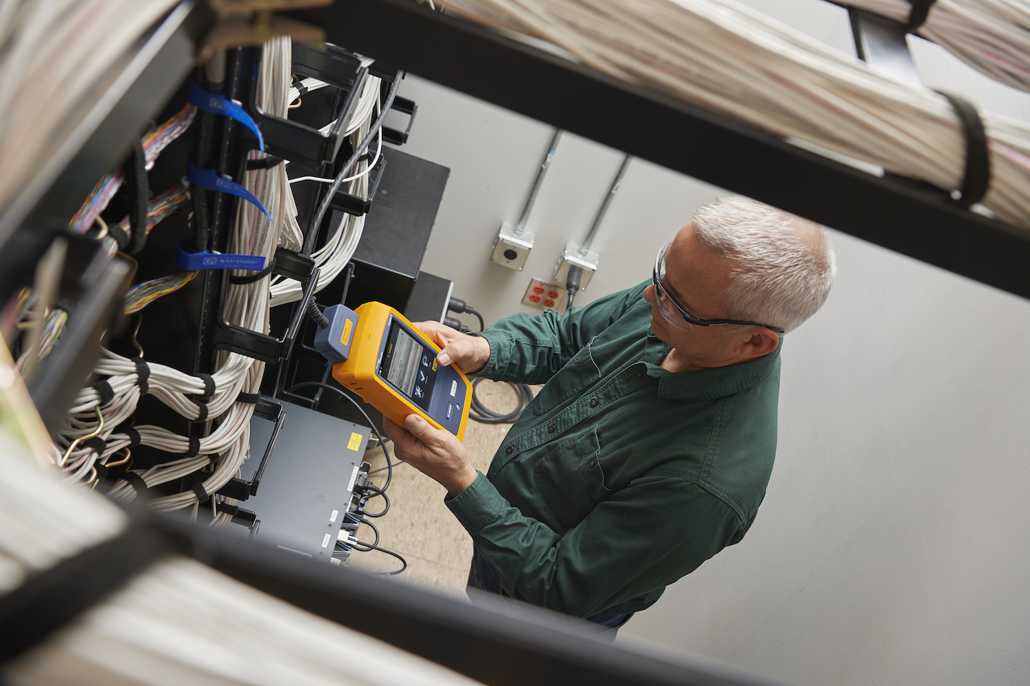 Man standing in a server room, holding a yellow cable testing device