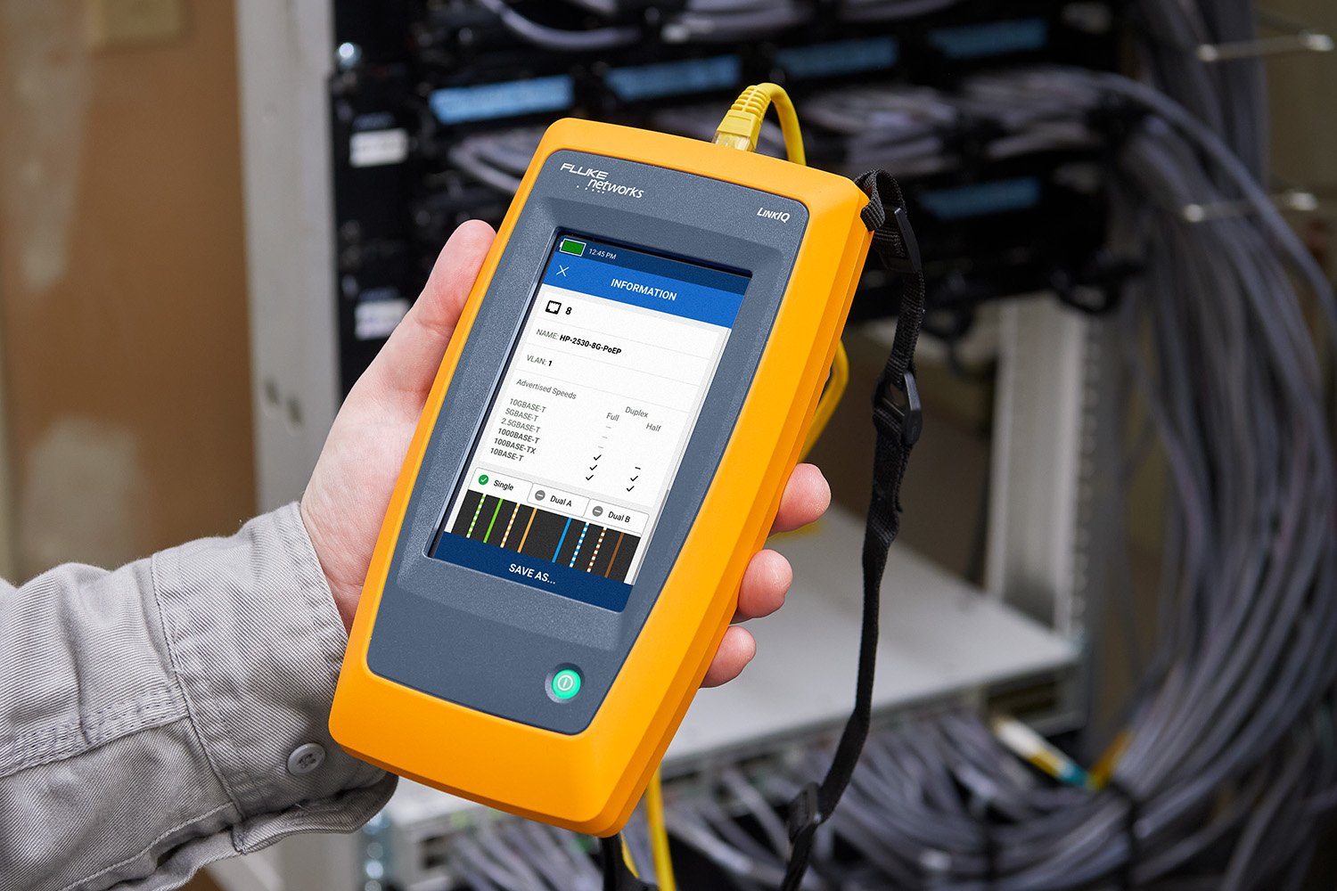 Technician’s hand holding a Fluke Networks LinkIQ in front of cable switches